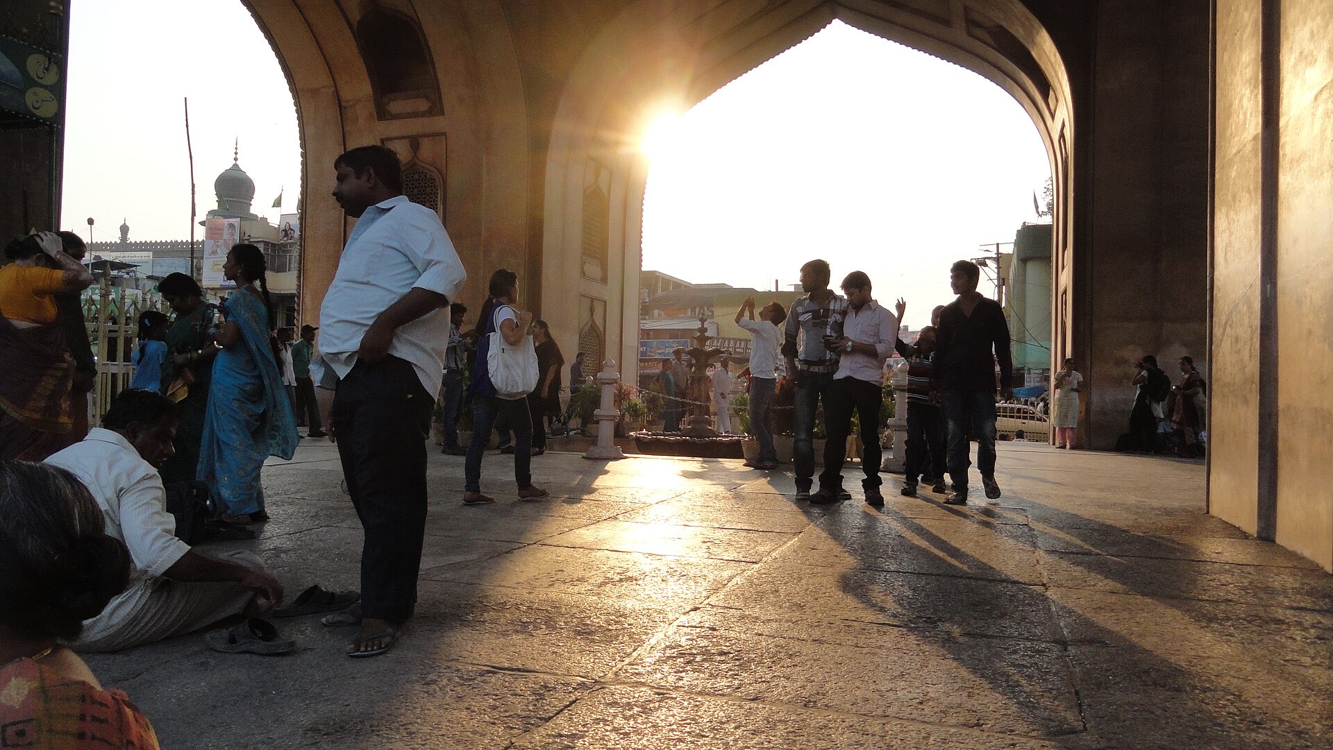 Sunset blazing through the grand arch of the Charminar, people silhouetted on the stone floor