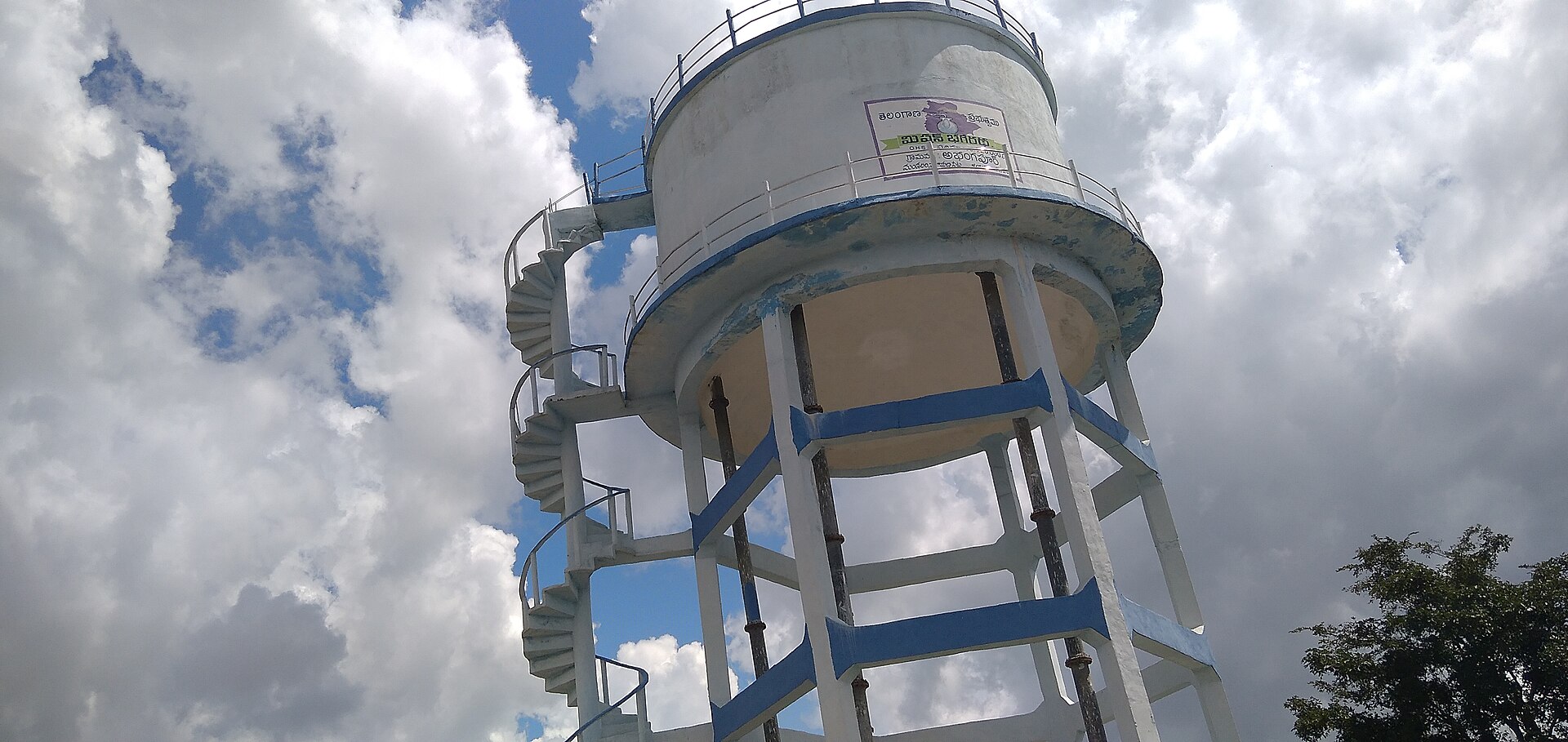A Mission Bhagiratha village water tank against a monsoon sky